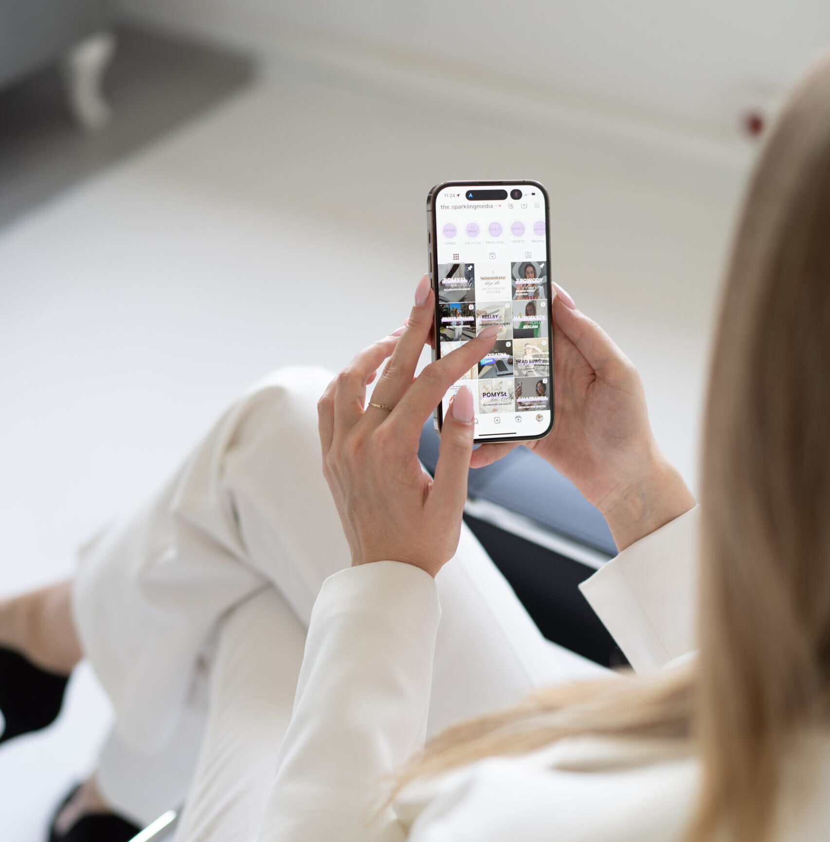 Aagmara Grzeszczuk z The Sparkling Media od marketingu dla architektów siedzi na czarnym metalowym krześle i w dłoniach trzyma smartfona.