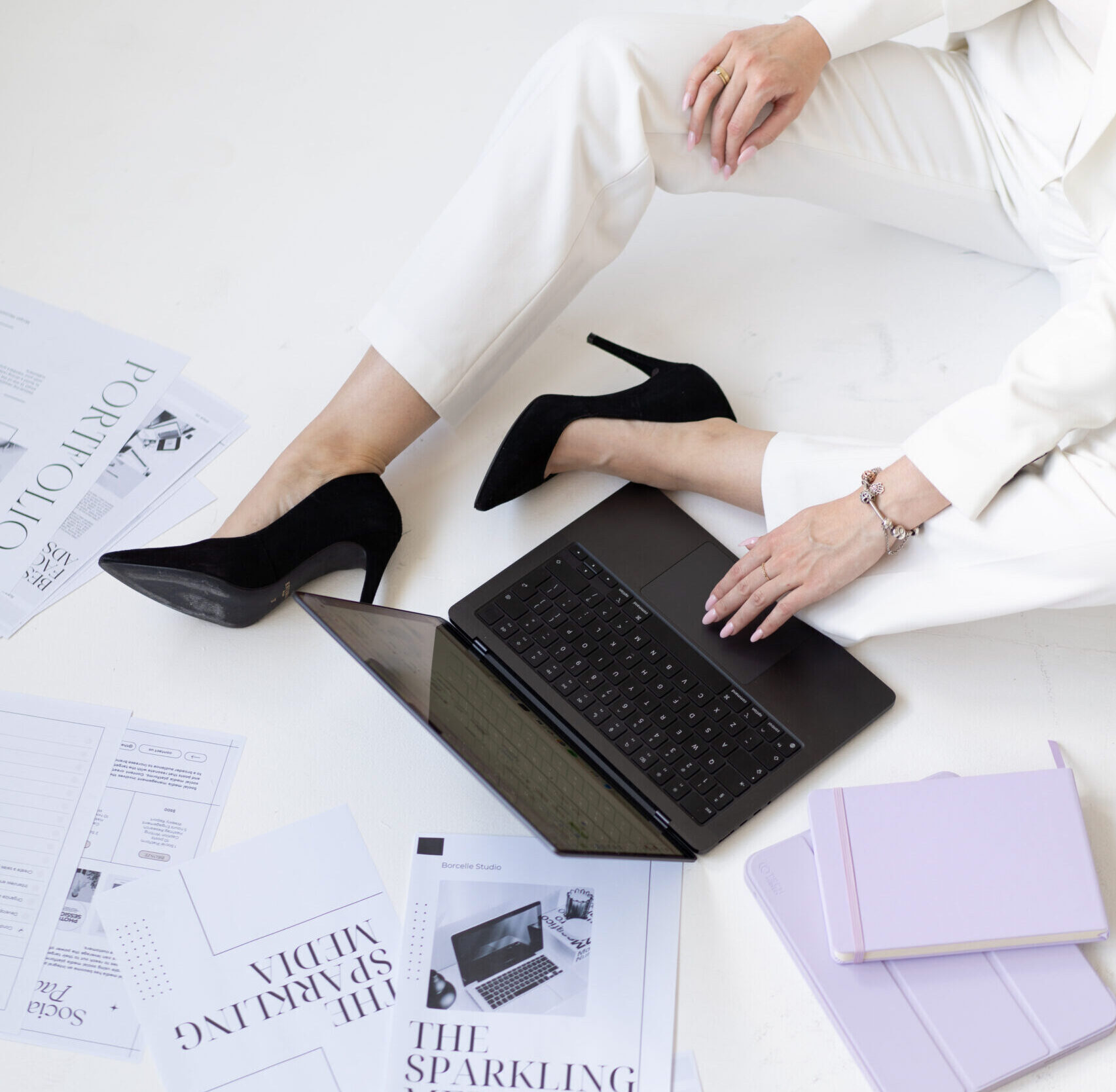 Dagmara Grzeszczuk z The Sparkling Media od marketingu dla architektów siedzi na ziemi w czarnych szpilkach. Obok leży laptop i kartki z logo firmy.